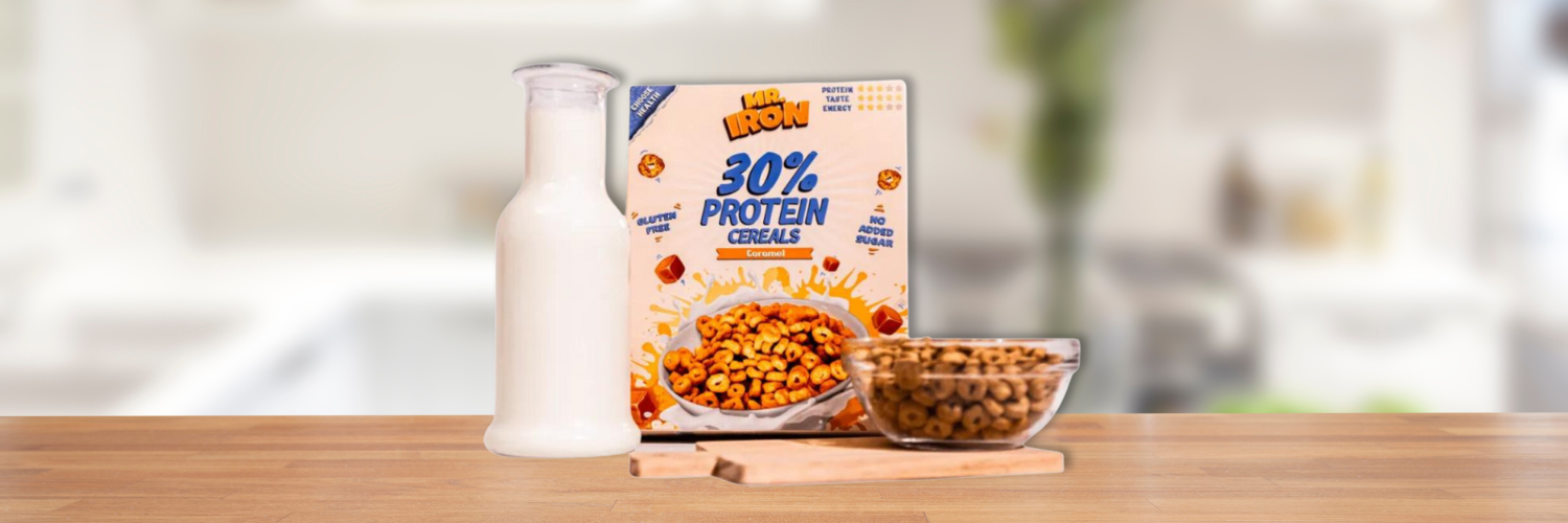 Cutie de cereale proteice Mr. Iron cu 30% proteine si aroma de caramel, fara gluten sau zahar adaugat, alaturi de o sticla de lapte si un bol plin, pe un blat de bucatarie.